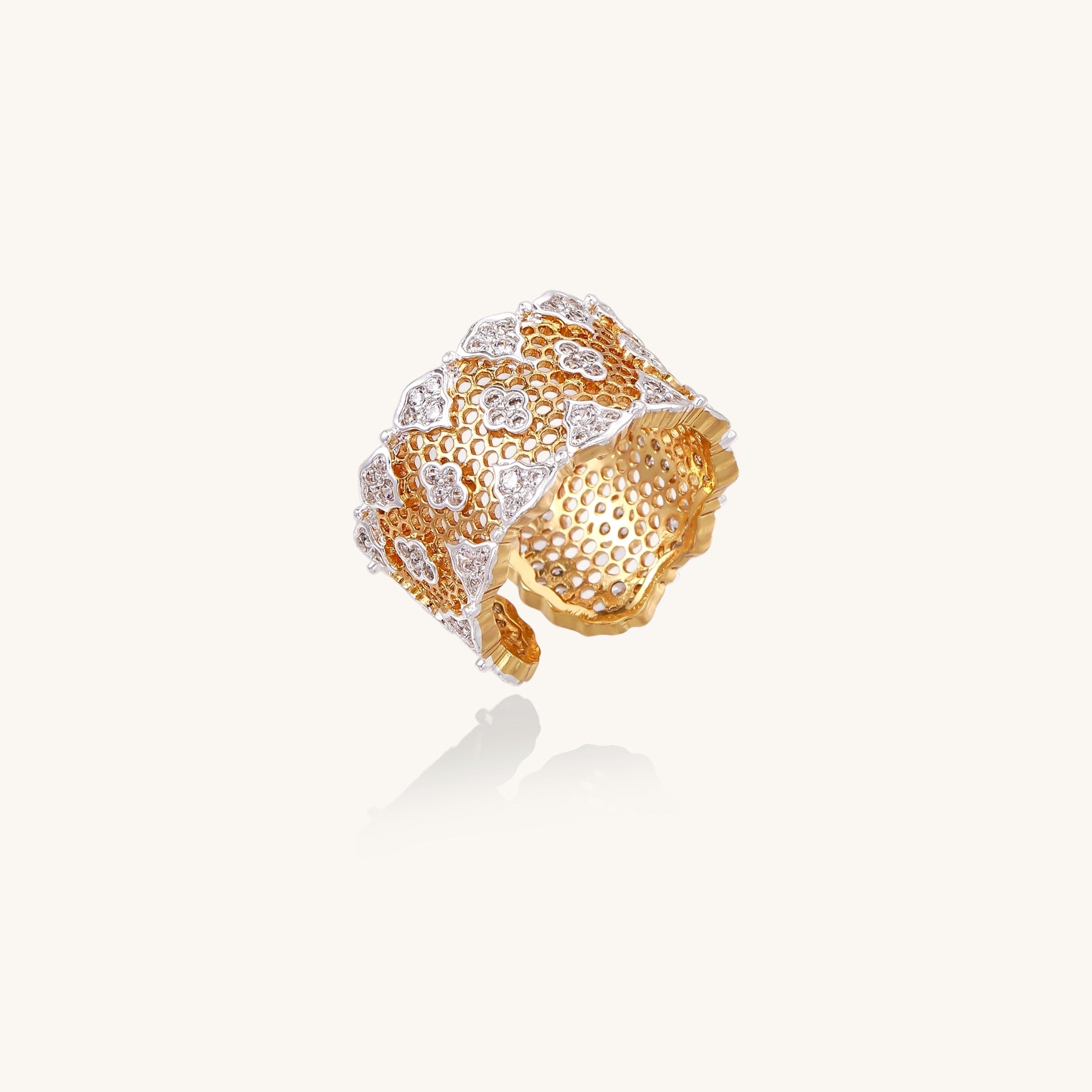 Wide gold-plated ring featuring intricate honeycomb mesh pattern with scattered zirconia stones on cream background