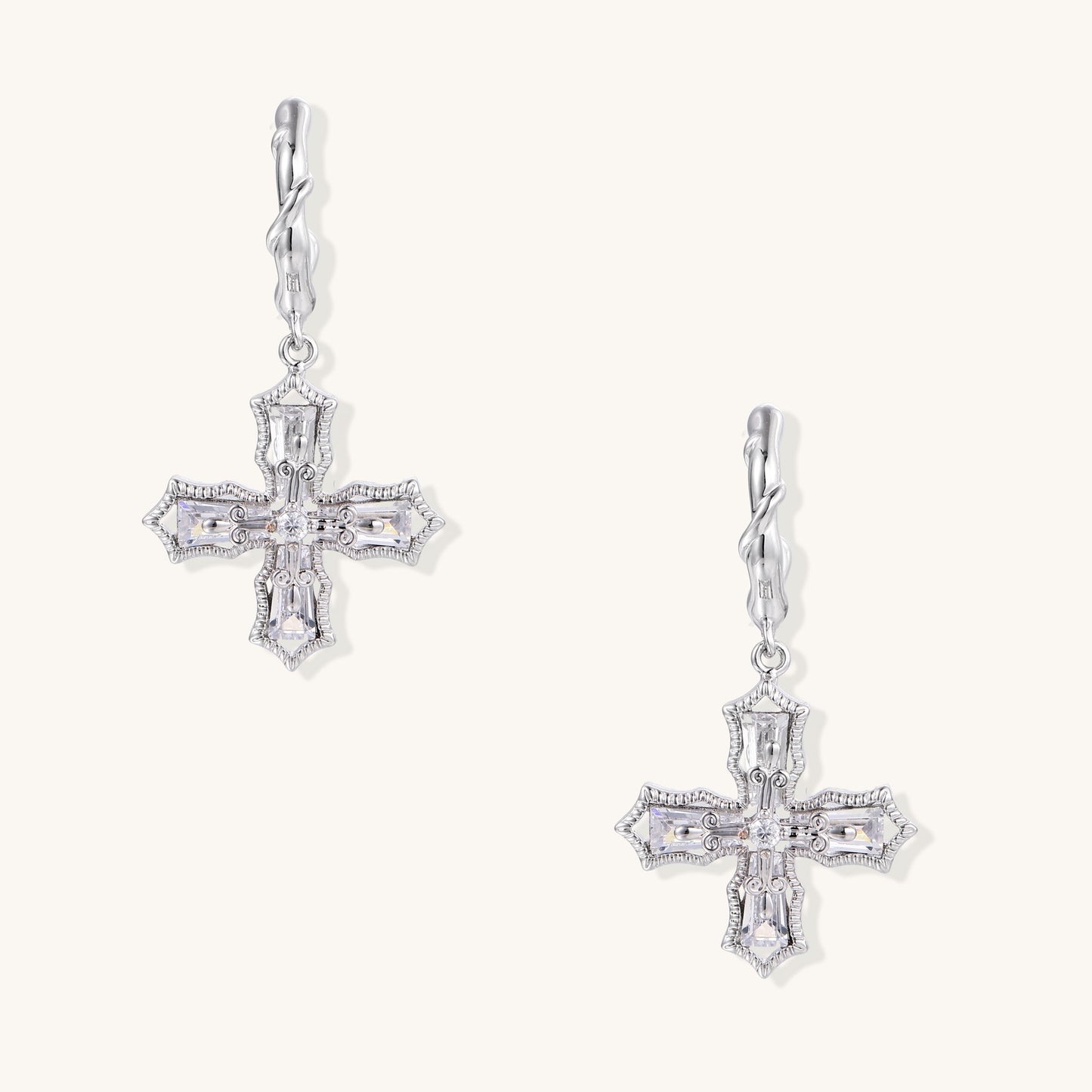 Ornate cross-shaped dangle earrings with gold plating and clear zirconia stones on beige background.